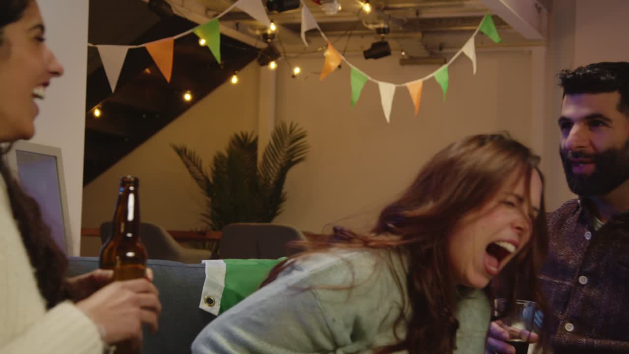 집이나 술집에서 친구 그룹이 성 패트릭의 날 파티에서 축하하고 알코올을 마시고 입으로 팝콘을 잡습니다.