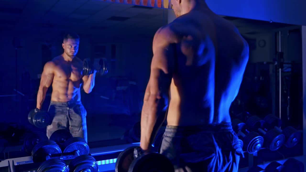 Bodybuilder che si allena in palestra. Bodybuilder forte e ben costruito che solleva pesi con manubri, preparandosi per l'esercizio in palestra.
