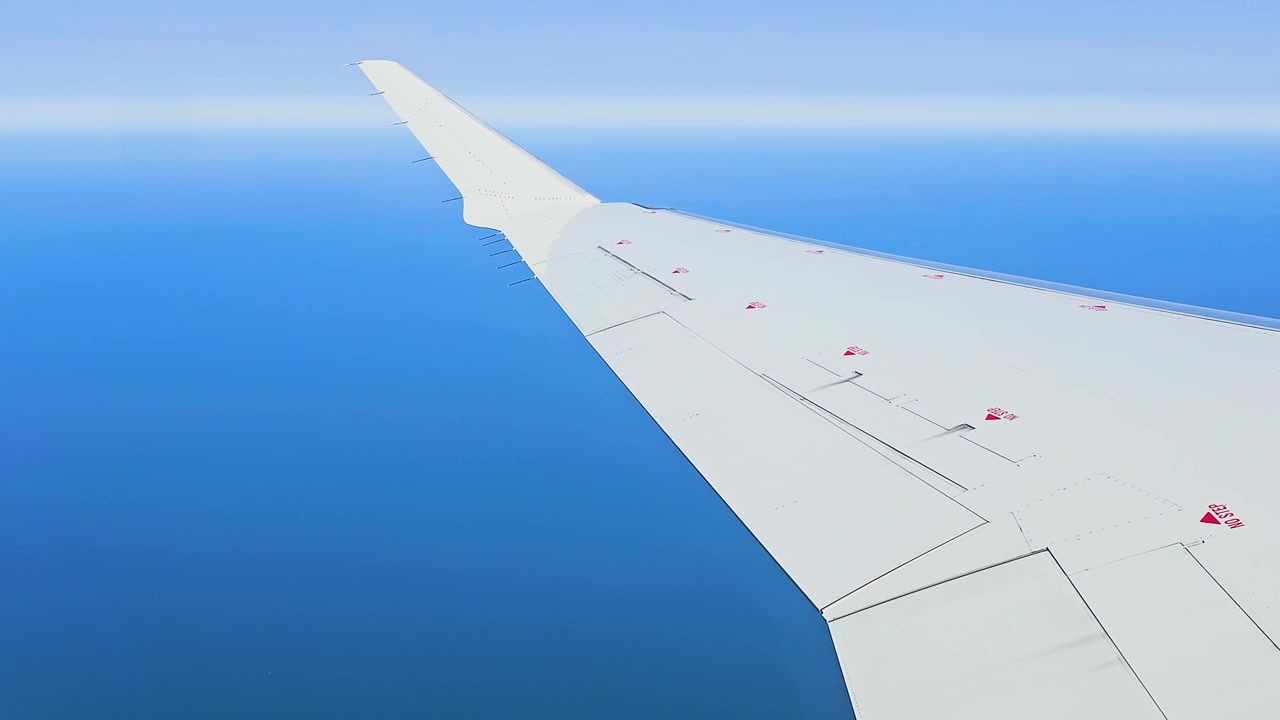 澄み切った青い海の上を飛ぶ旅客機の翼。遠くの水平線とクリアな空が広がる、高高度飛行中の飛行機の窓からの眺め。航空写真のような空撮視点で、夏の旅行や航空の背景に最適。