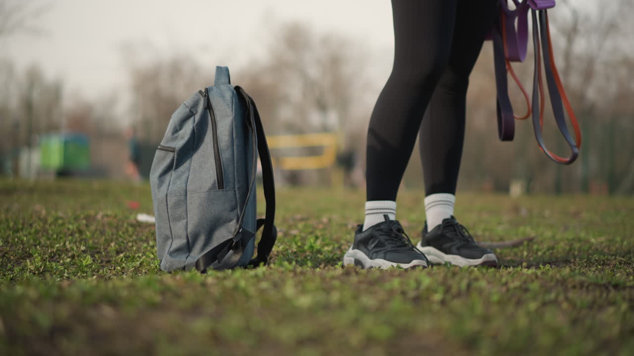 Closeup Of Walking, Photograph Captures Rhythmic Walking With Backpacks Nearby And Trailing Leashes, Detailed Candid Shot Of Feet In Sneakers Crossing Textured Grass With Backpack And Trailing Leash