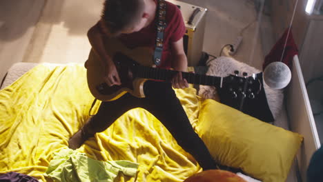 teenage boy playing electric guitar in his bedroom