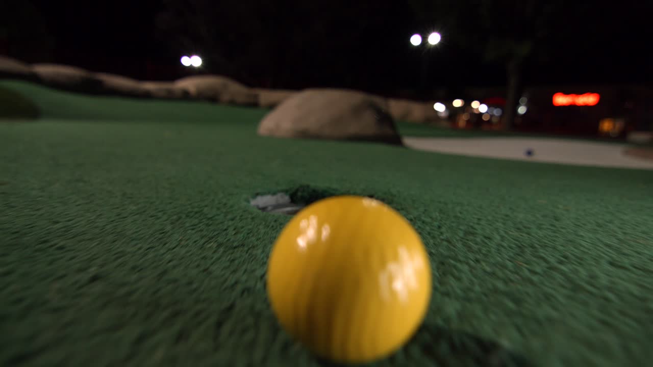 Una pallina da minigolf gialla cade nella buca da golf e rimbalza nella tasca su un campo.