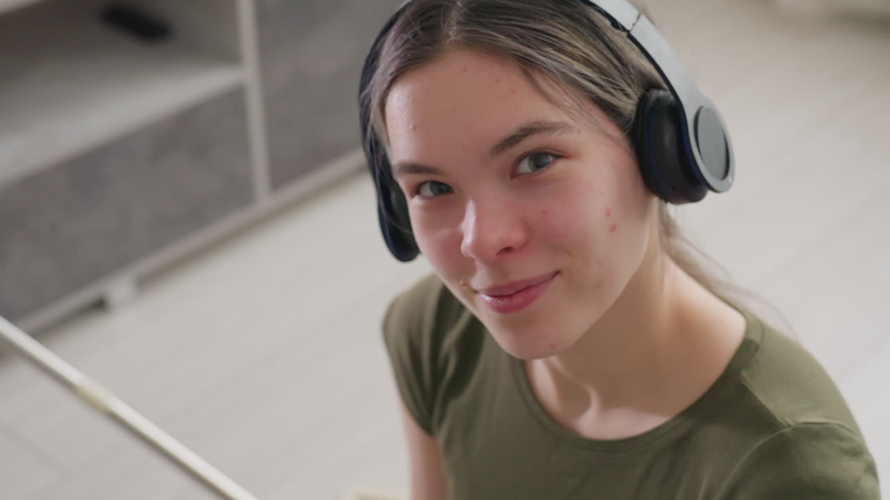 Overhead view of young girl wearing headphones looking upward while dancing to rhythm of music, closed eyes and subtle movements showing enjoyment, natural light