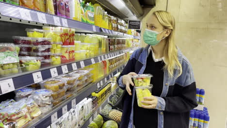 mulher de máscara a comprar frutas cortadas no supermercado.