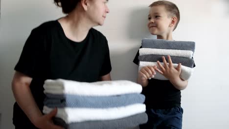 woman and a boy standing near walls, holding stacks of different towels. family concept.