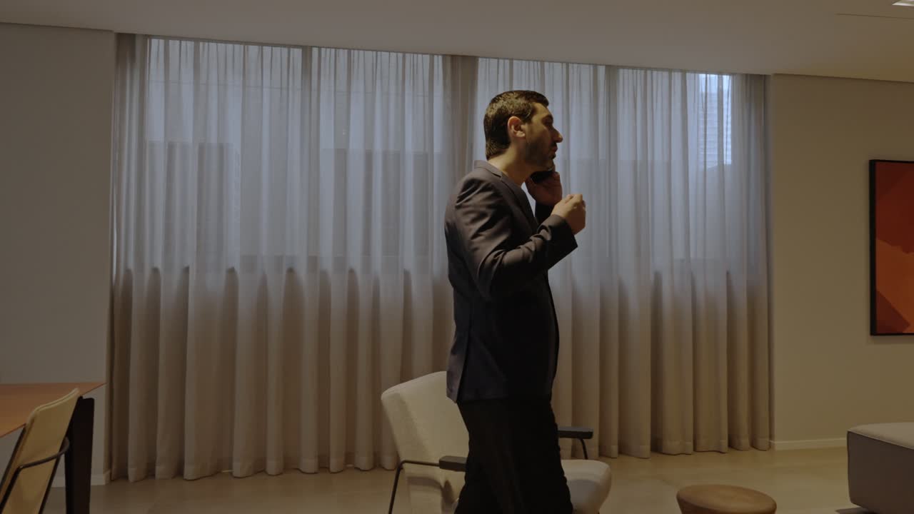 Executive man walking confidently while talking on the phone inside a modern meeting room with elegant decor.