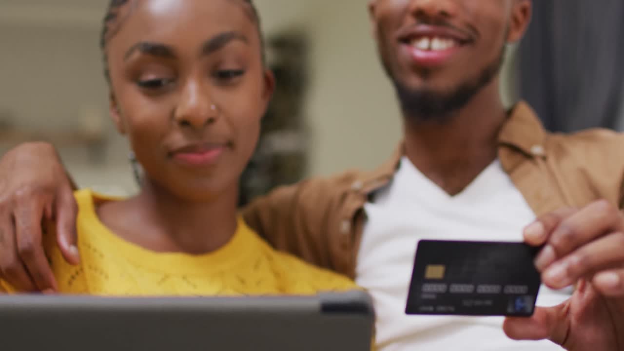 Joyeux couple afro-américain assis sur un canapé et faisant des achats en ligne