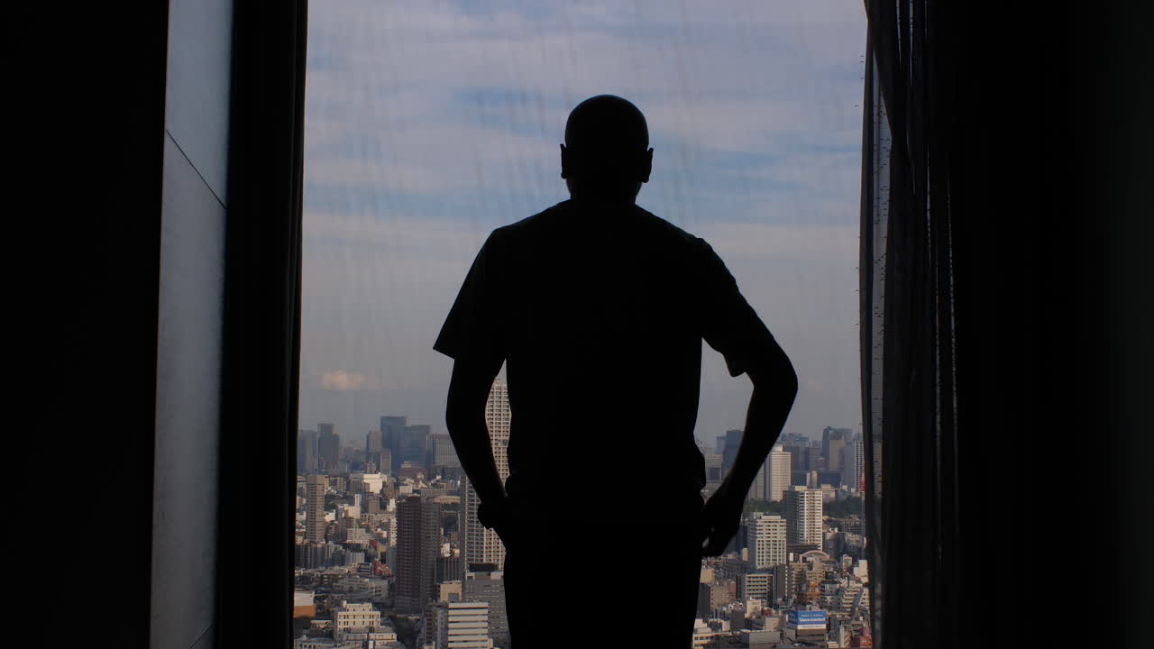 la silueta de un hombre caminando hacia una gran ventana en un edificio de gran altura y abriendo cortinas para revelar la vista expansiva de la metrópolis de la ciudad
