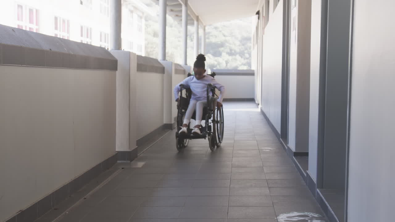 Navigating school hallway, African American girl in wheelchair moving independently