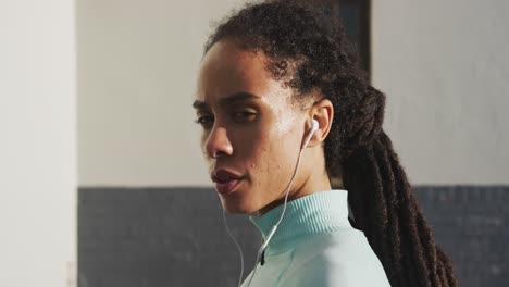 Portrait-of-african-american-woman-in-sportswear-wearing-earphones-on-a-sunny-day