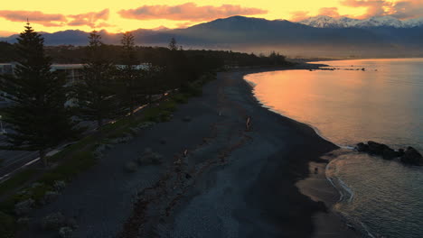 tiro de dron del mar al atardecer con fondo de montaña cubierto de nieve y cielo naranja