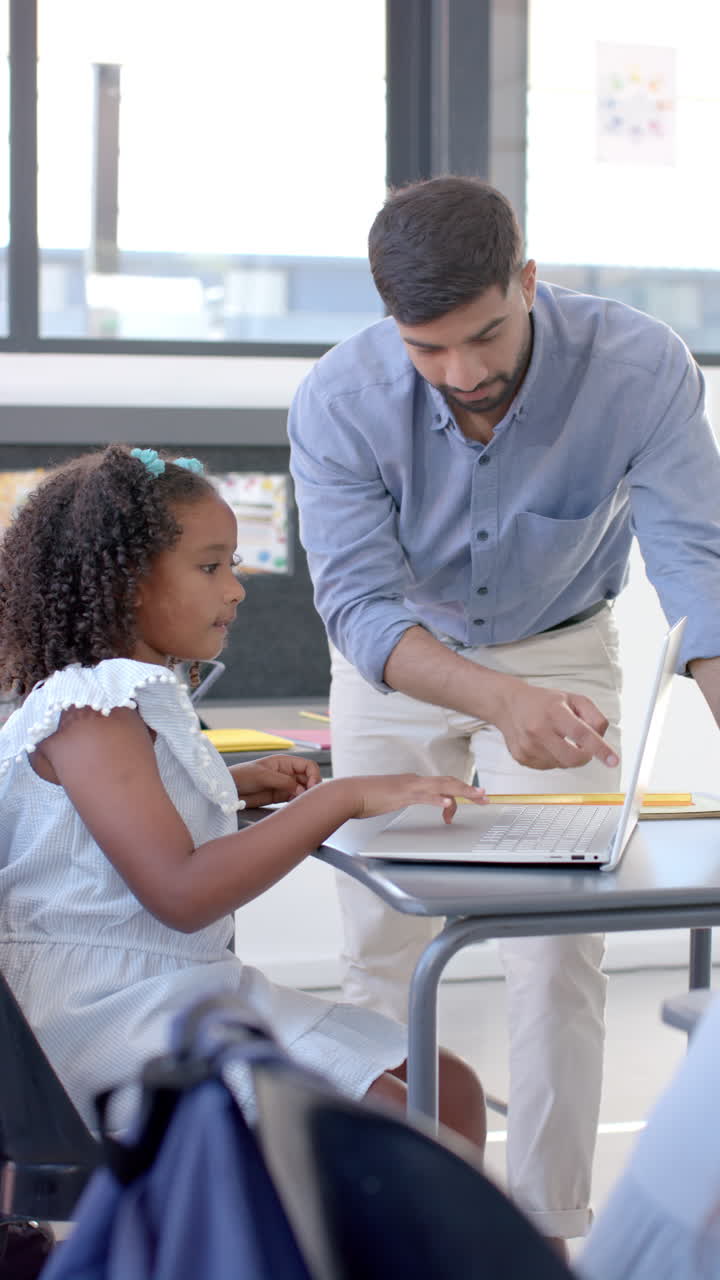 Vertical video: In school, teacher helping student using laptop in classroom, focusing on learning