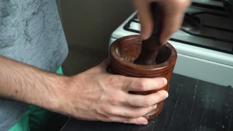 man grinding spices and black pepper on wooded mortar with pestle