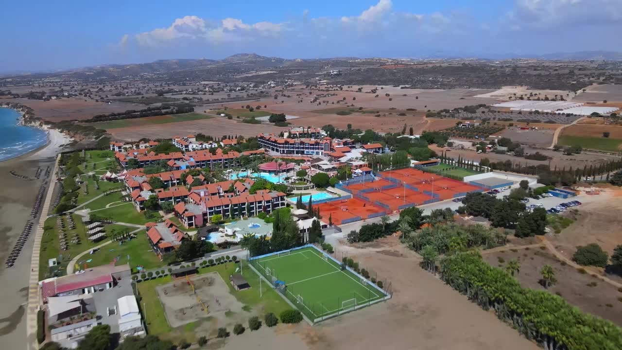 Drone video of Ksamil, Albania, showcasing a breathtaking curved beach, red-tiled villas, and lush coastal farmland. Captivating aerial footage offers stunning bird's-eye views and vibrant hues