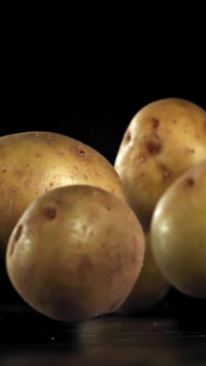 Patate fresche e crude che cadono al rallentatore su sfondo nero