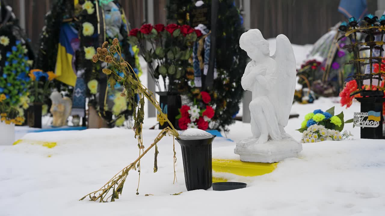 On a cold winter day, a faded bouquet of flowers rests in front of an angel statue, honoring a fallen Ukrainian soldier at Irpin Cemetery, Ukraine, who died in the Ukraine-Russia war.