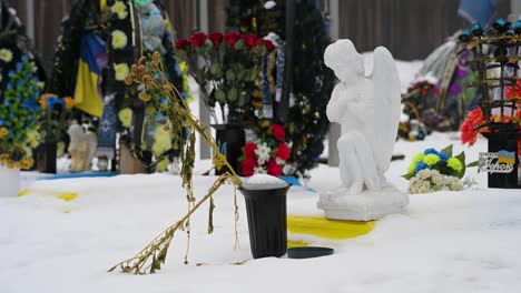 on a cold winter day, a faded bouquet of flowers rests in front of an angel statue, honoring a fallen ukrainian soldier at irpin cemetery, ukraine, who died in the ukraine-russia war.