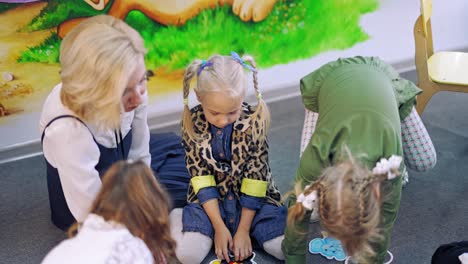teacher sits together with children on carpet at school. little kids learning english words while sitting on the floor in the classroom.