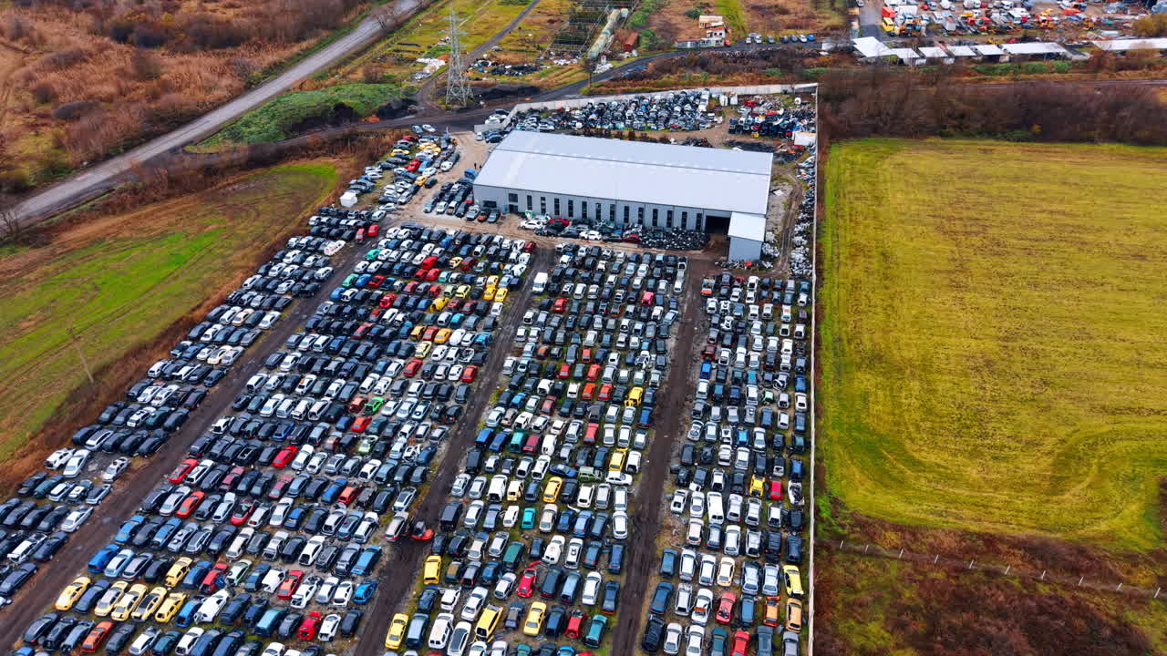 Ampia vista aerea di uno sfasciacarrozze con magazzino industriale. Ripresa con drone ad alta quota di un grande deposito di auto rottamate con un edificio di magazzino vicino a campi verdi e strade.