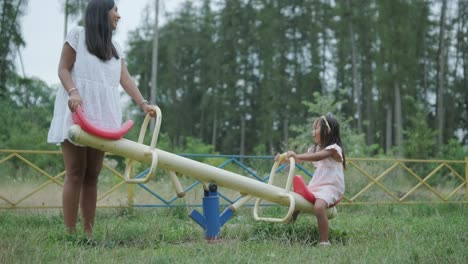 a pregnant mother and her young daughter enjoy playful time together at a playground in the park, surrounded by trees and greenery