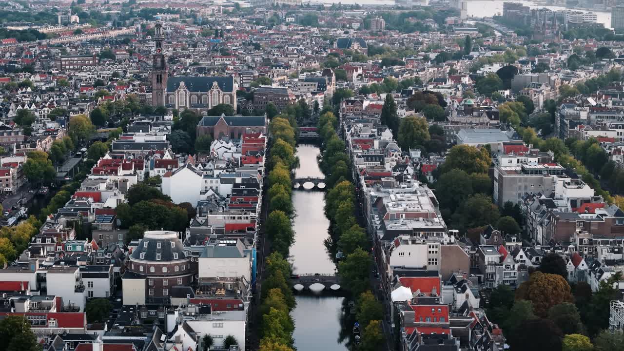 Drone dolly left above Amsterdam canals at sunrise, long shadows and golden early light, establishing panoramic city