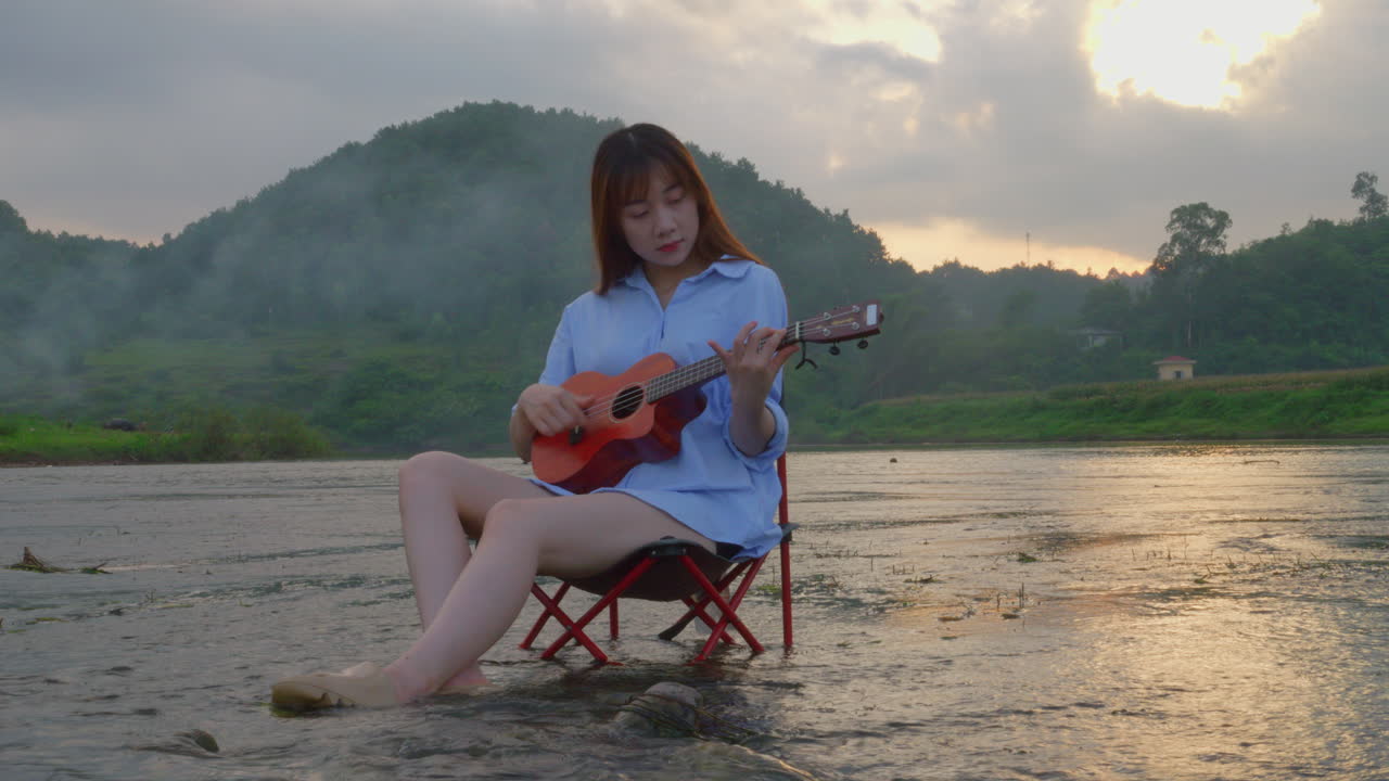 Woman playing ukulele in river at sunset