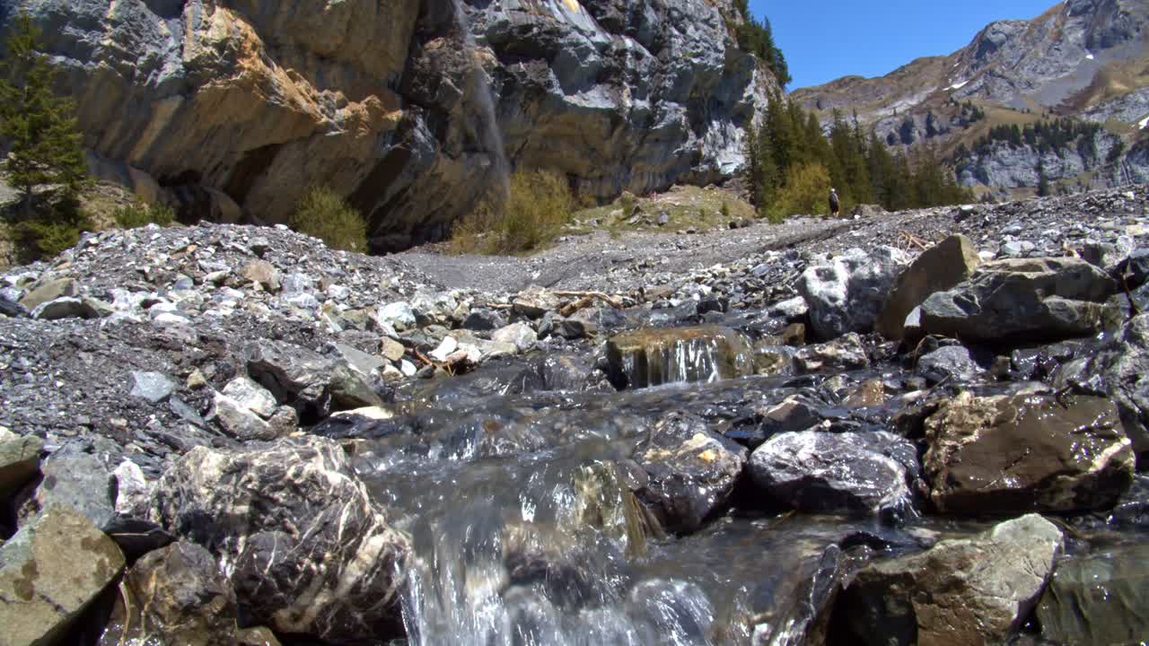 cerca de un riachuelo que fluye por un lecho rocoso, la cascada detrás le da vida
