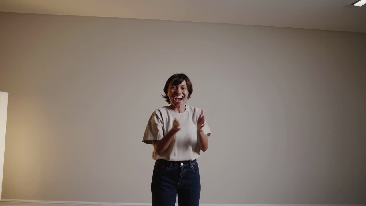 Una donna applaude gioiosamente in una stanza minimalista. Lo scatto grandangolare cattura la sua energia, perfetto