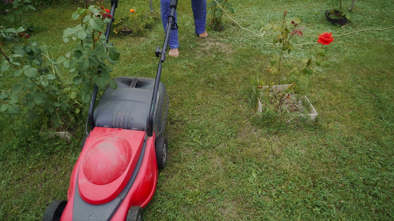 Barefoot young girl uses lawn mower to mow a lawn in garden. Close Up of mowing the lawn