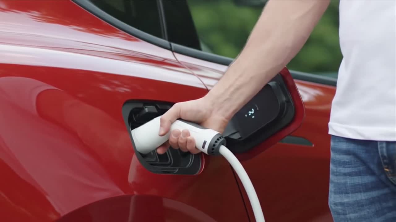 Kişi, güç kablosunu takarak kırmızı bir elektrikli aracı şarj ediyor.
