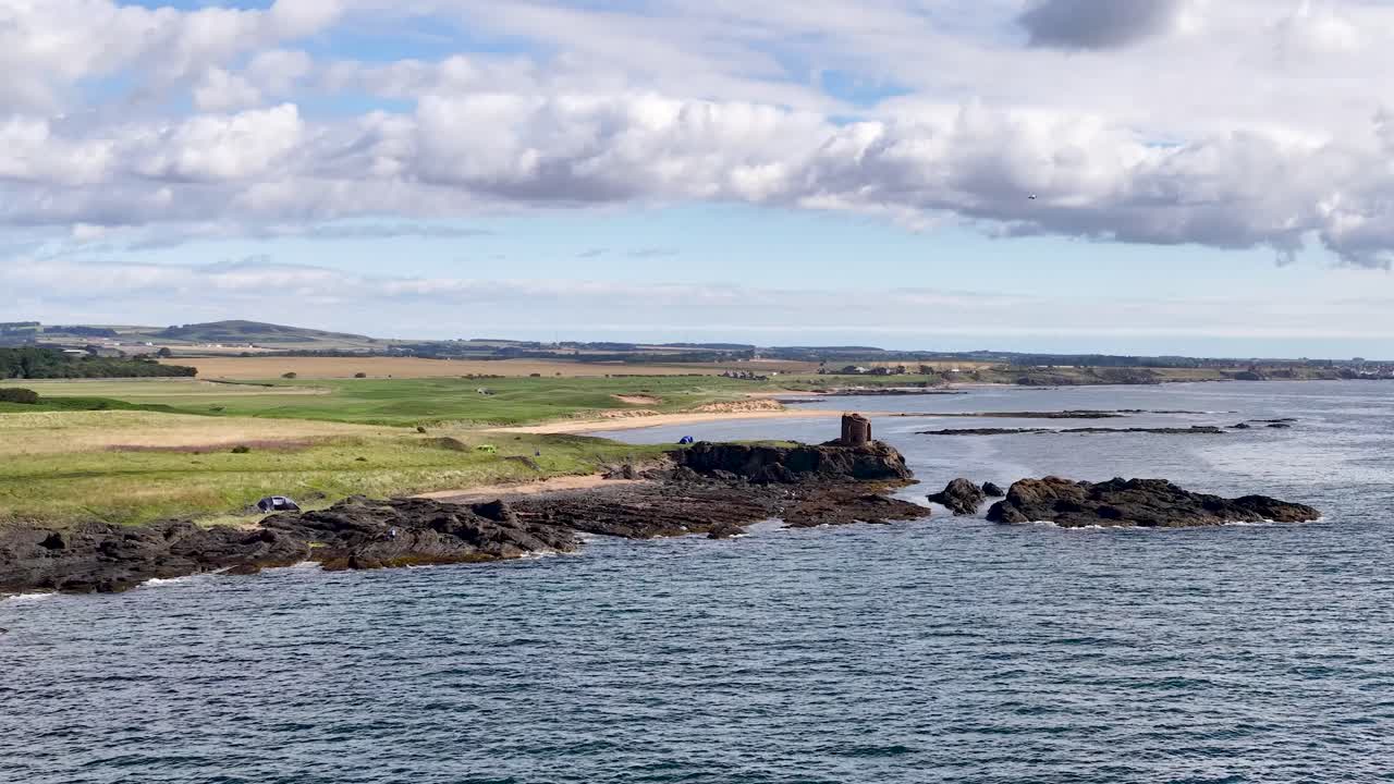 Slow pan reveals ancient stone ruins on rocky coast under bright daylight and scattered clouds