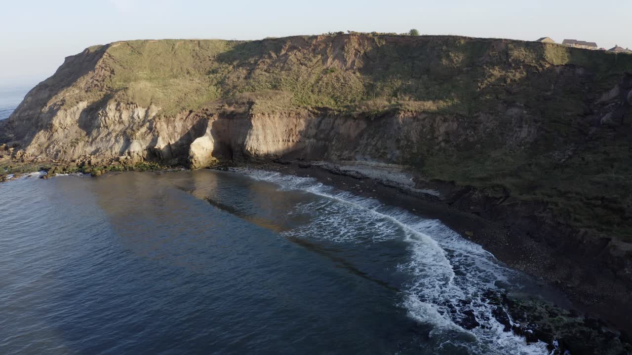 Aerial rising view of cliffs and sea revealing coastal resort, Scarborough England UK