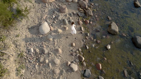 Top-down---A-woman-in-a-white-dress-approaches-the-rocky-shore