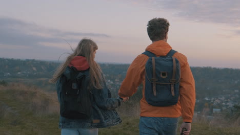 young male and female hikers with backpacks reaching the top of the mountain