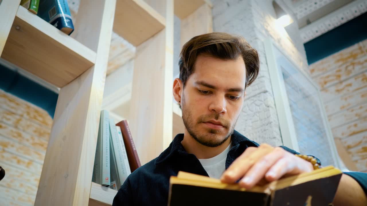 un joven está leyendo un libro cerca de una estantería. elige un libro para comprar.