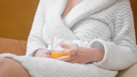 mujer hermosa en bata blanca relajándose en el sofá con un vaso de jugo