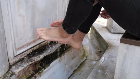 muslim man washes his feet while performing ablution at the mosque fountain, people perform their religious rituals