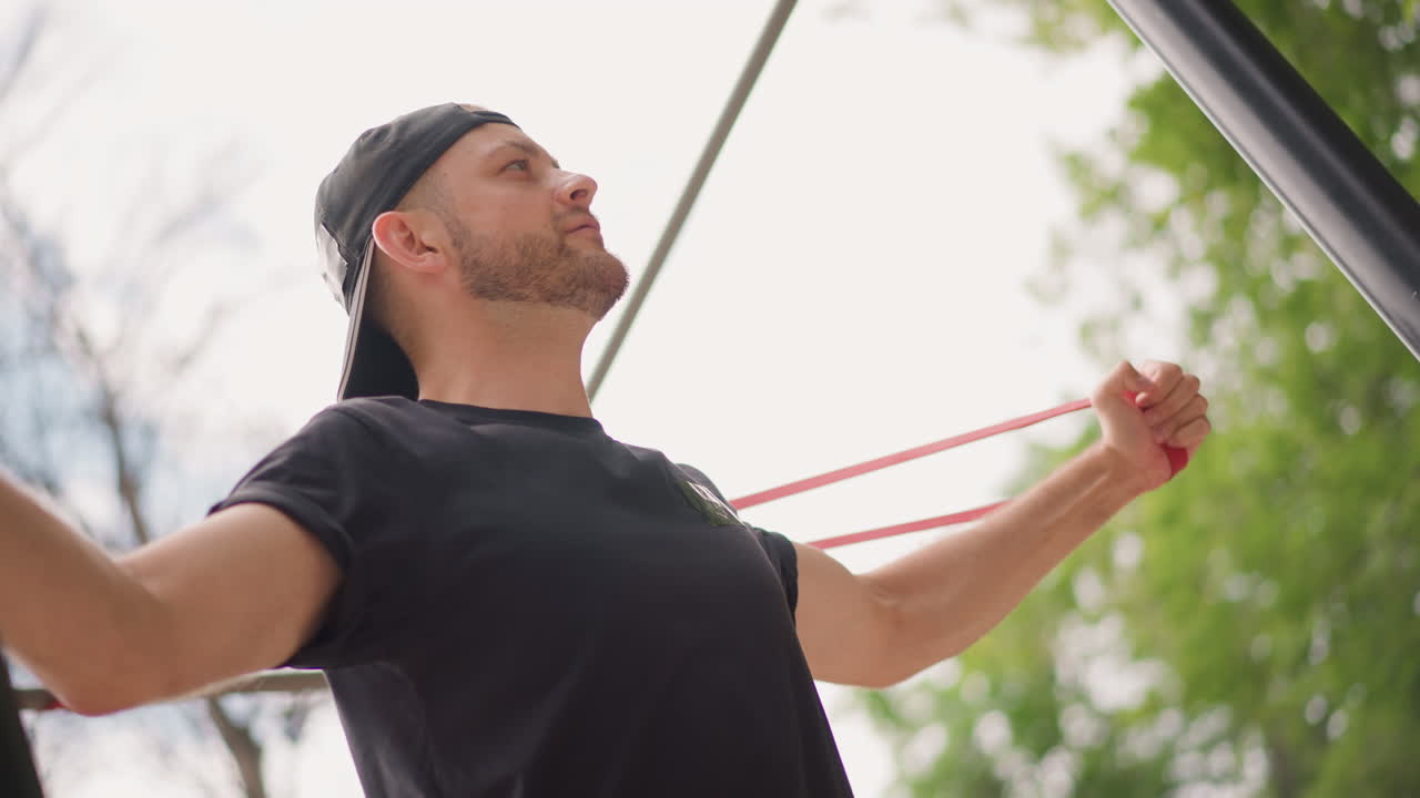 Man Exercises Outdoors, Person Practicing Resistance Training For Chest In Open Park Setting, Individual Doing Resistance Band Chest Exercise In Park With Attentive Focus And Regular Breathing