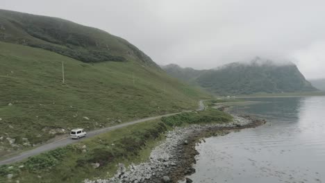drone tracking shot of a campervan on a single track road during a trip of the scotland north coast 500 with a loch and cloudy topped mountains in view