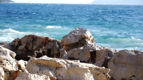 Nahaufnahme-Von-Schäumenden-Wellen-Der-Adria,-Die-Gegen-Die-Felsige-Küste-Eines-Albanischen-Strandes-Krachen