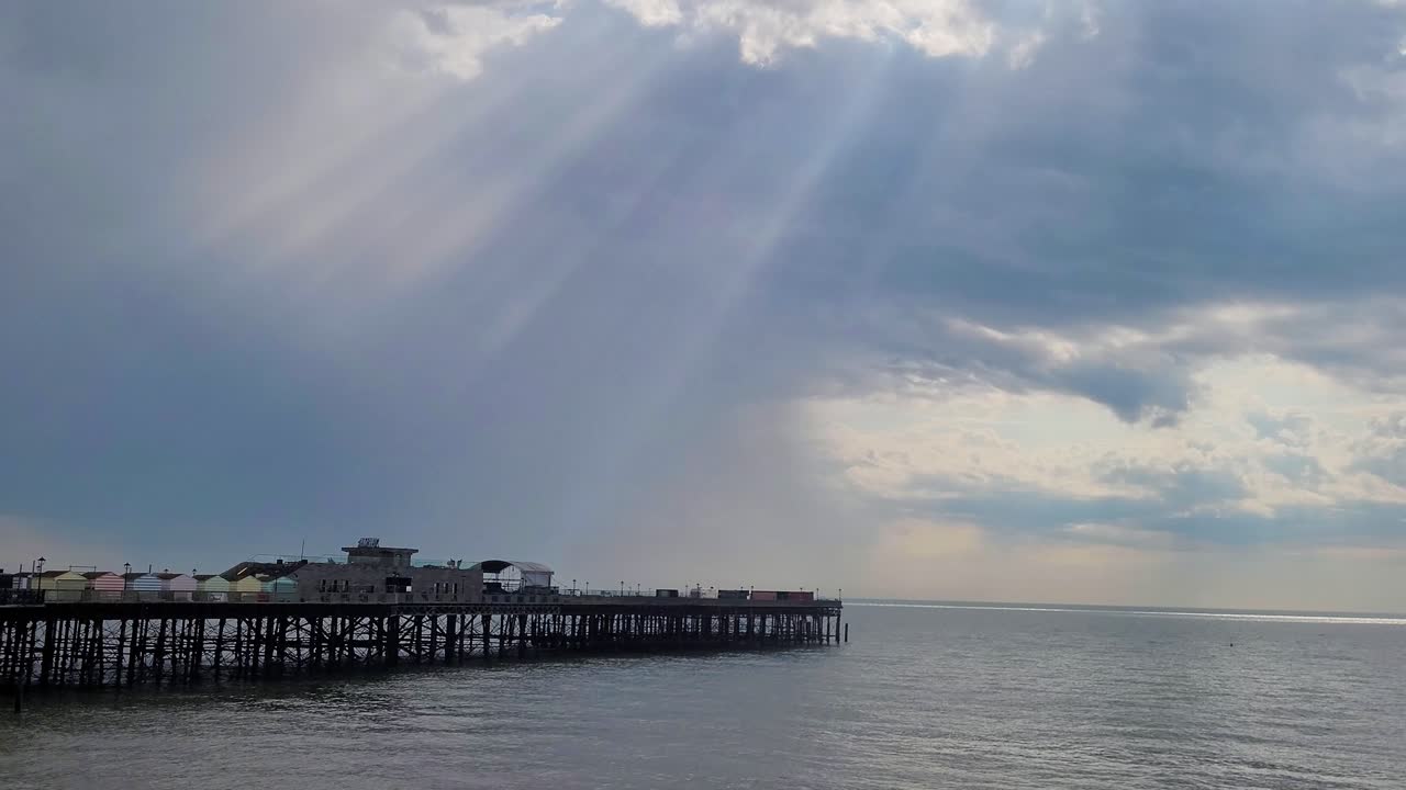 Hastings pier on a cloudy day with God rays peaking through, with the horizon in the background
