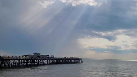 hastings pier on a cloudy day with god rays peaking through, with the horizon in the background