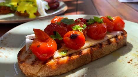 Deliciosa-Tostada-De-Masa-Fermentada-Bruschetta-Con-Tomates-Cherry-Y-Albahaca-Fresca,-Desayuno-Tradicional-Italiano-En-Un-Restaurante,-Toma-De-4k