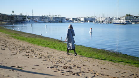 a healthy old woman with a walking stick for her disability getting exercise and enjoying the beach in newport, california slow motion