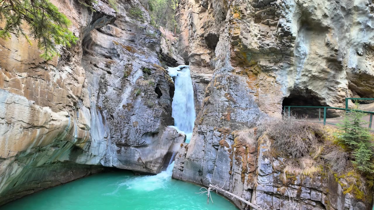 Kayalık bir kanyonun içinde turkuaz buzul göletine dökülen şelalenin manzaralı görünümü.