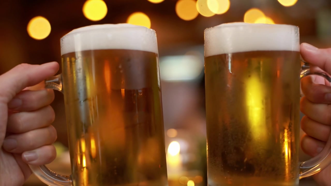 Primo piano di due mani che brindano con boccali di birra in un bar