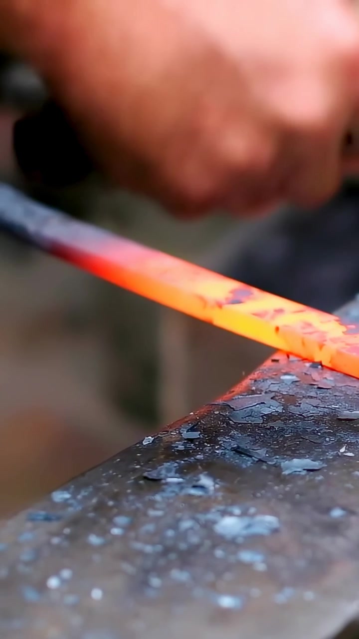 Vertical video: Placing hot tip onto bench, smith in short sleeves hammering and forging steel bar