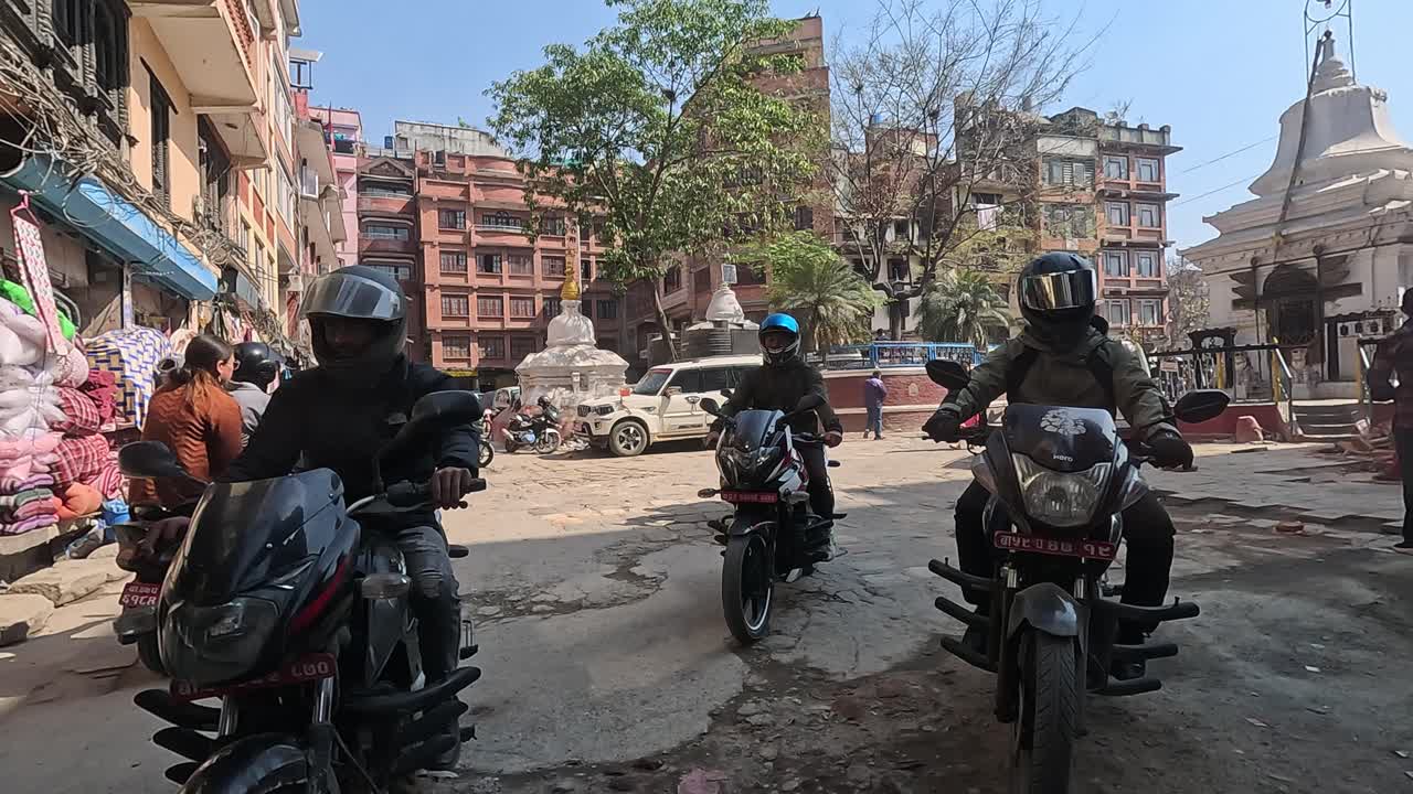 Backseat view of a car navigating the lively alleys of central Kathmandu, following motorbikers in a dynamic urban commute. Thamel area full of stores and narrow alleys
