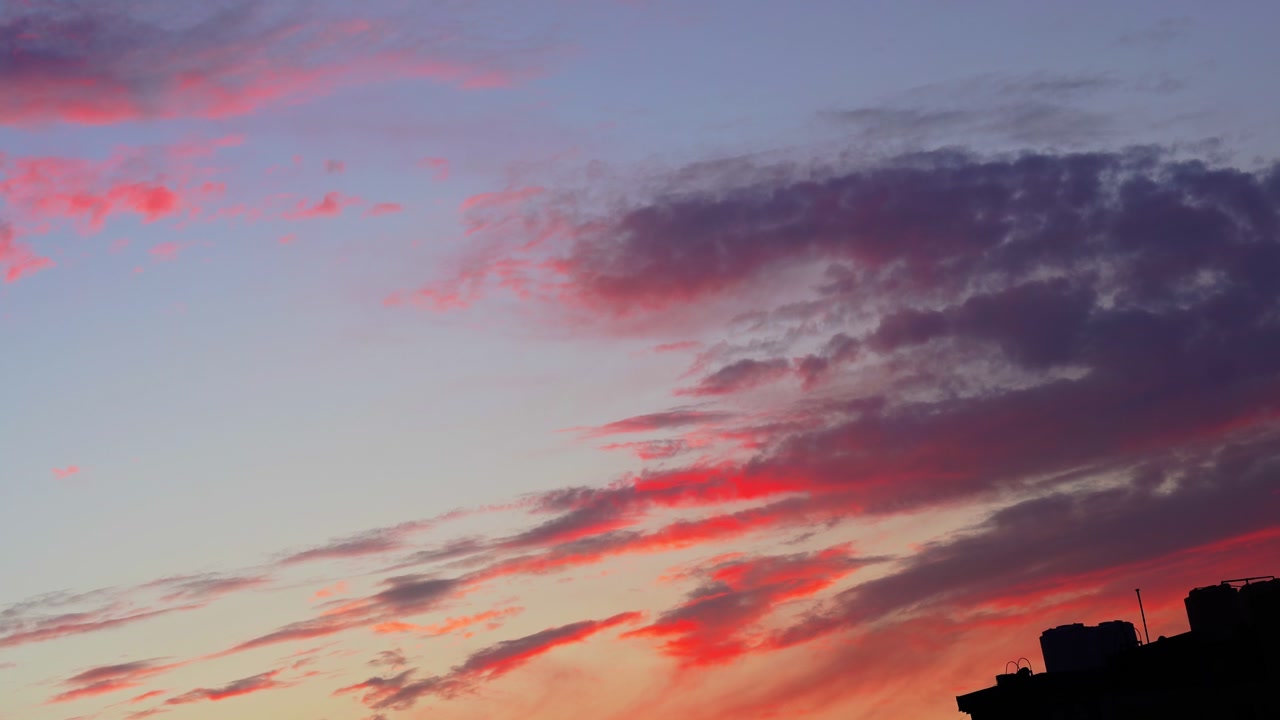 Dramatic pink and orange clouds drift across the twilight sky over a dark city silhouette. This beautiful natural background is perfect for cinematic transitions and atmospheric storytelling.