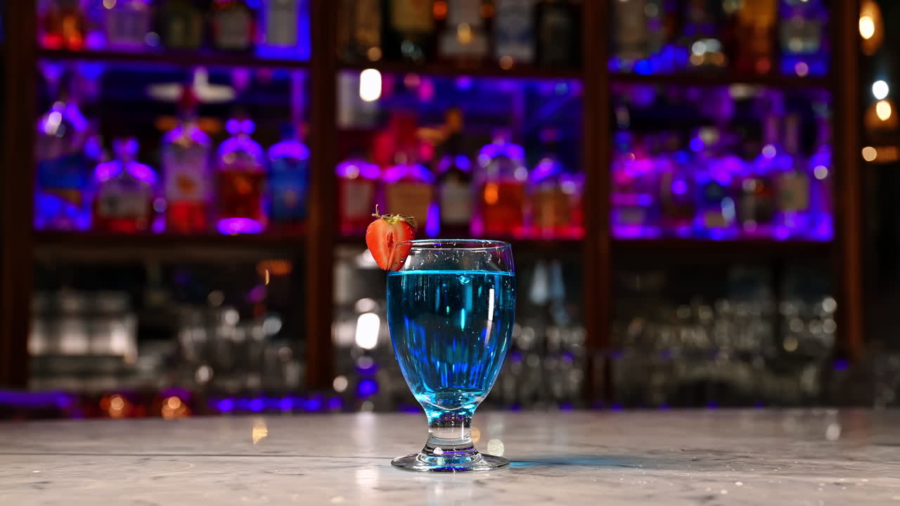 Blå cocktail med jordbærskive i moderne bar. Frisk blå cocktail med jordbærpynt på bardisk med neon lilla og blå belysning.